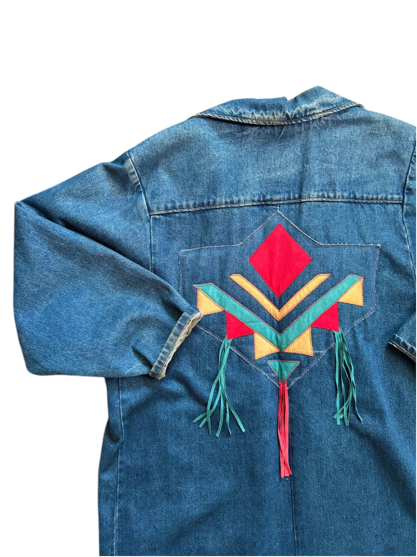 Back view of a denim trench jacket with a colorful geometric pattern and tassel detail on the back. 1980s Pioneer Wear denim trench with Aztec pattern, rare vintage find from Everythang Dope.