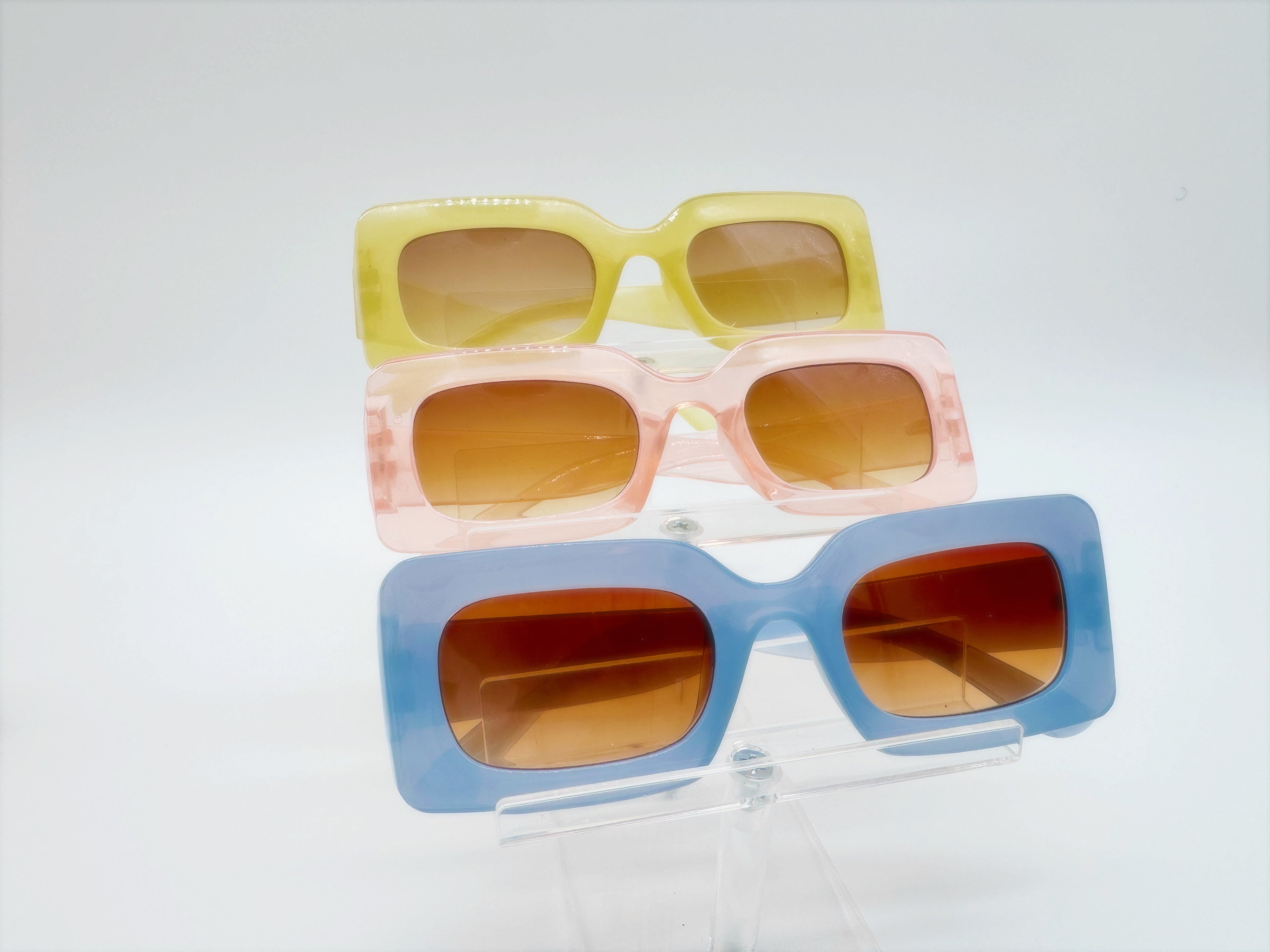 Three pairs of square-framed sunglasses in yellow, pink, and blue colors displayed against a white background.