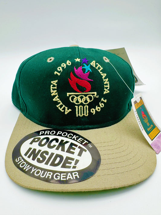 A vintage 1996 Atlanta Olympics cap with green and beige colors, featuring the Olympic rings and the text 'ATLANTA 1996' on the front.